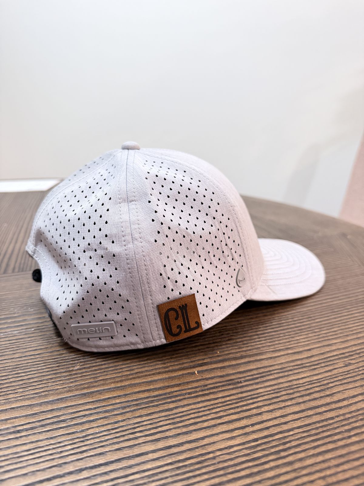 Performance trucker cap on a wood table finished with a small leather monogram patch reading C L