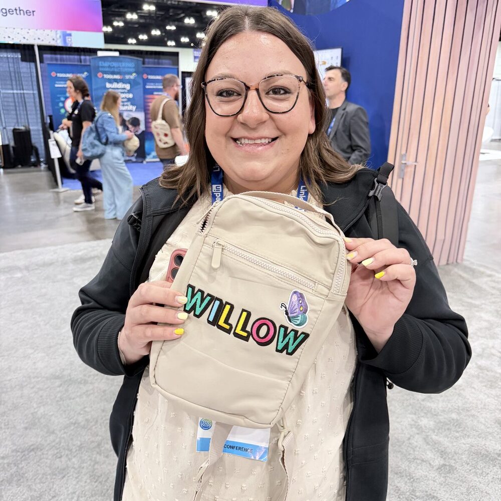 Smiling guest holding up a cream sling bag personalized with the name Willow in colorful embroidered lettering